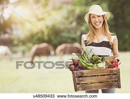 Stock Image - Woman carrying fresh vegetables in box. Fotosearch