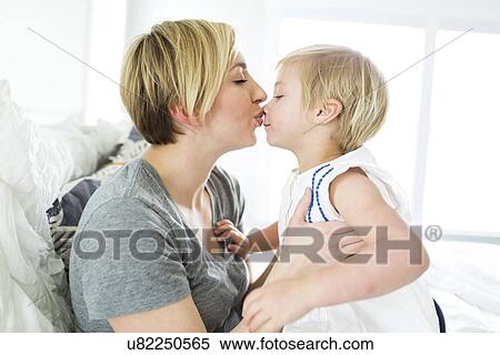 Stock Photography - Woman kissing girl (2-3) in bedroom. Fotosearch