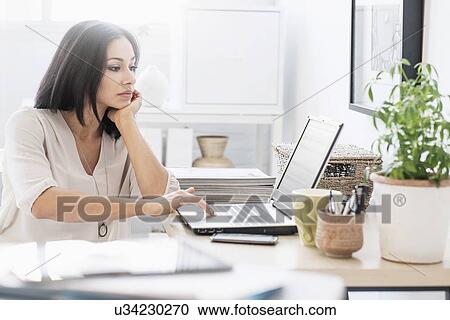 Stock Image - Woman sitting at desk with laptop. Fotosearch