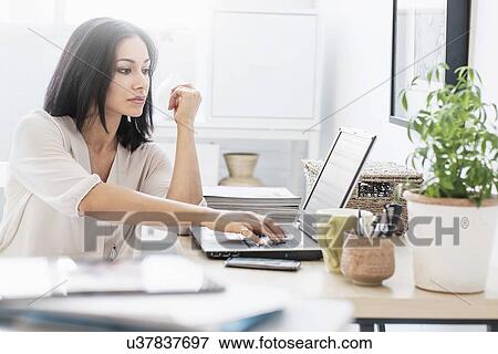 Stock Photo - Woman sitting at desk with laptop. Fotosearch