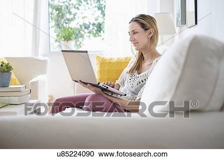 Stock Image - Woman with laptop sitting on sofa . Fotosearch