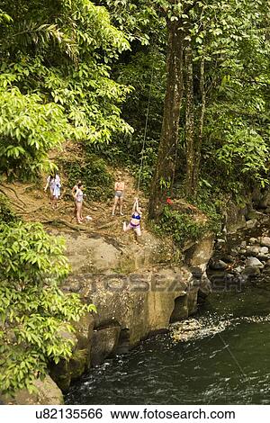 Stock Photograph - Women swinging on rope swing above river in distance. Fotosearch