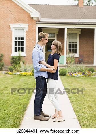 Stock Image - Young couple standing on footpath in front of house. Fotosearch
