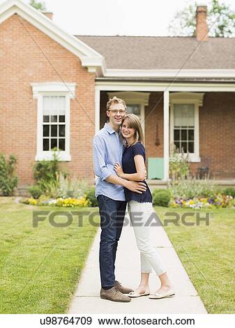 Young couple standing on footpath in front of house View Large Photo Image Stock Photo - Young couple standing on footpath in front of house. Fotosearch