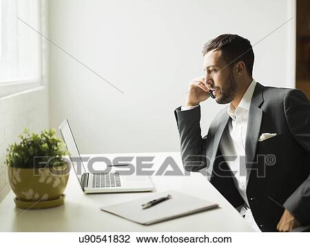 Stock Image - Young man sitting at desk and looking at laptop. Fotosearch