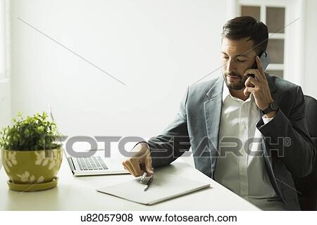 Stock Photo - Young man sitting at desk and looking at laptop. Fotosearch