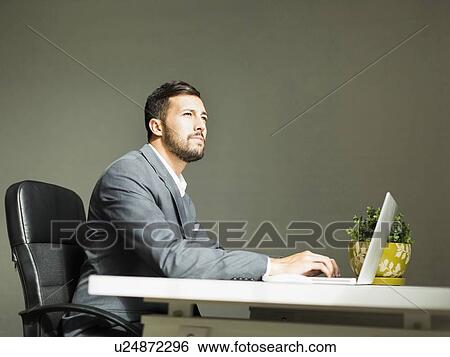 Stock Photograph - Young man sitting at desk and using laptop. Fotosearch