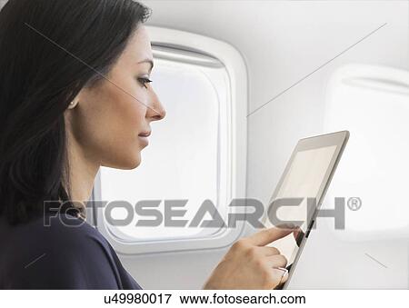 Stock Photo - Young woman using tablet on plane. Fotosearch