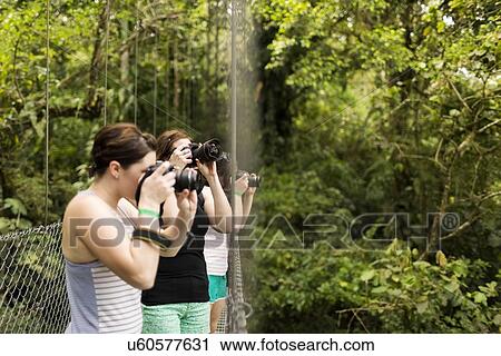 Stock Image - Young women photographing in forest. Fotosearch