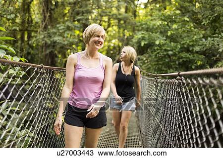 Young women walking on footbridge in forest View Large Photo Image Stock Image - Young women walking on footbridge in forest. Fotosearch