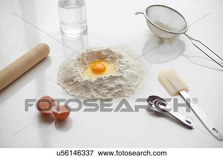 Stock Photo - Baking preparation with raw egg in center of flour stack and kitchen utensils. Fotosearch