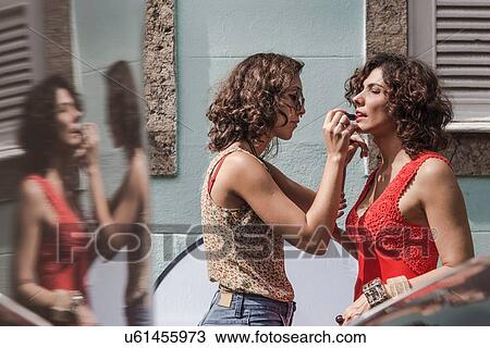 Stock Image - Behind the scenes of an urban fashion shoot with make up artist applying lipstick to model. Fotosearch