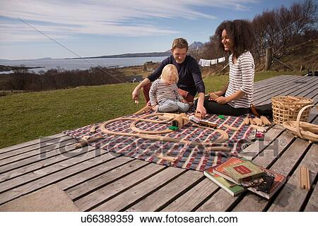 Stock Photo - Boy and parents playing with toy train on wooden decking. Fotosearch