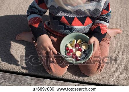 Stock Image - Boy holding bowl of fruit, high angle. Fotosearch