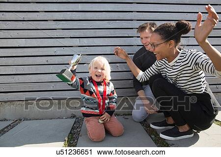 Stock Image - Boy holding trophy, mother cheering. Fotosearch