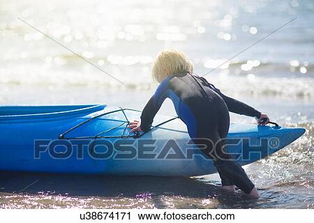 Stock Image - Boy in water pushing canoe. Fotosearch