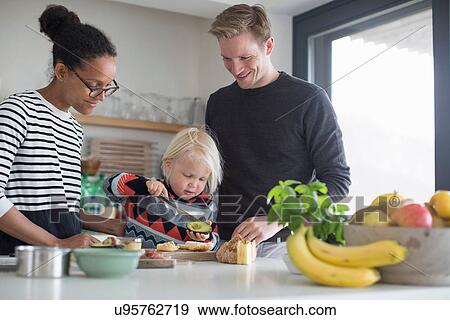 Stock Photo - Boy preparing food in kitchen with parents. Fotosearch