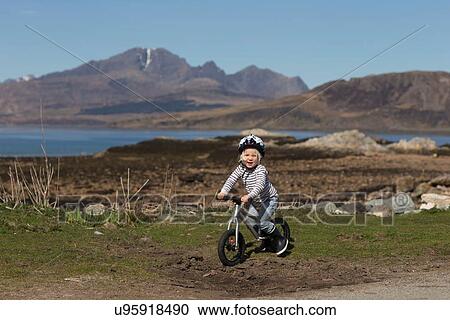 Stock Image - Boy riding bike, Lake Eishort, Isle of Skye, Hebrides, Scotland. Fotosearch