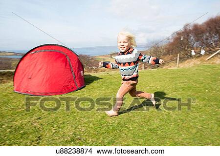Picture - Boy running on grass with tent. Fotosearch