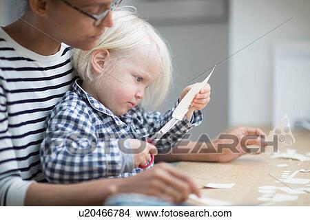 Boy using scissors to cut paper with his mother View Large Photo Image Picture - Boy using scissors to cut paper with his mother. Fotosearch