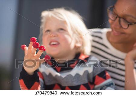 Stock Image - Boy with raspberries on fingers, mother watching. Fotosearch