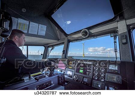 Stock Photo - Captain of boat steering through offshore wind farm. Fotosearch