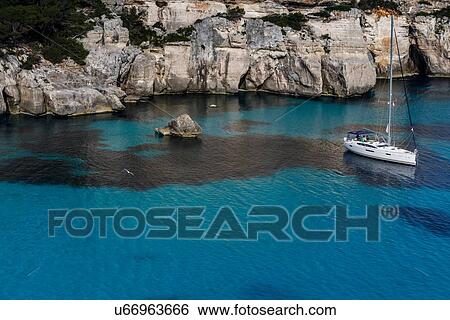 Stock Photograph - Cliffs of Cala Macarella and sailboat, Menorca, Spain. Fotosearch