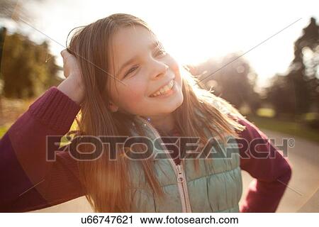 Stock Image - Close up of girl with hand in hair in sunlit park. Fotosearch