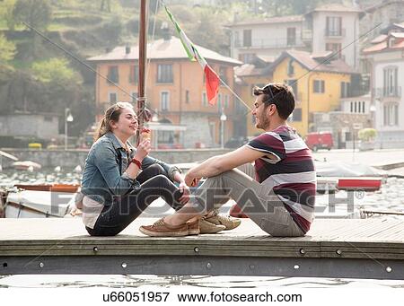 Stock Photo - Couple sitting on pier eating ice cream cone at lake Mergozzo, Verbania, Piemonte, Italy. Fotosearch