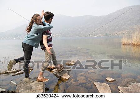 Picture - Couple stepping on rocks at Lake Mergozzo, Verbania, Piemonte, Italy. Fotosearch