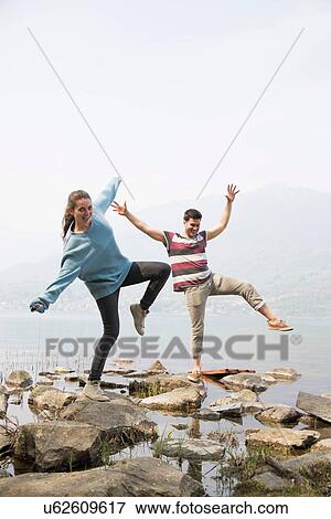 Couple stepping on rocks with arms raised at Lake Mergozzo, Verbania, Piemonte, Italy View Large Photo Image Stock Photo - Couple stepping on rocks with arms raised at Lake Mergozzo, Verbania, Piemonte, Italy. Fotosearch
