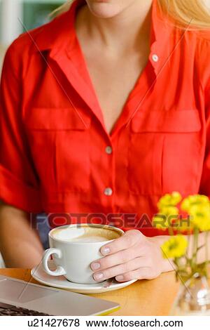 Stock Photo - Cropped close up of young woman in cafe drinking coffee whilst using laptop. Fotosearch
