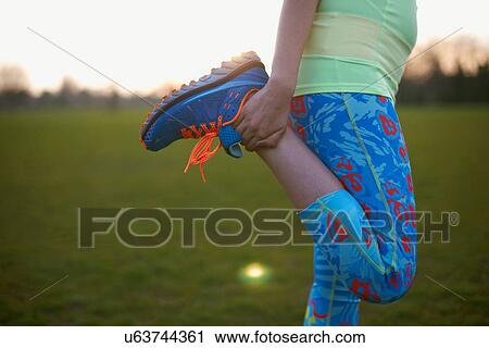 Stock Image - Cropped image of woman stretching leg for exercise in park. Fotosearch