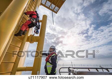 Stock Photo - Engineer climbing wind turbine at offshore windfarm. Fotosearch