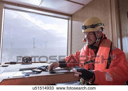 Stock Image - Engineer on boat making notes on digital tablet at offshore windfarm. Fotosearch