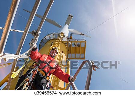 Picture - Engineer preparing to climb windturbine at offshore windfarm, low angle view. Fotosearch