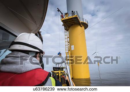 Stock Photo - Engineers winching parts up to wind turbine on offshore windfarm. Fotosearch