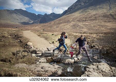Stock Image - Family crossing stream, Fairy Pools, Isle of Skye, Hebrides, Scotland. Fotosearch
