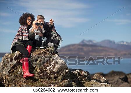Stock Image - Family sitting on rocks, boy using binolculars. Fotosearch