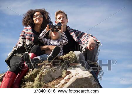 Family sitting on rocks, boy using binolculars View Large Photo Image Stock Photograph - Family sitting on rocks, boy using binolculars. Fotosearch