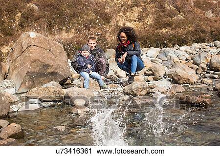Stock Image - Family throwing stones in pond, Fairy Pools, Isle of Skye, Hebrides, Scotland. Fotosearch