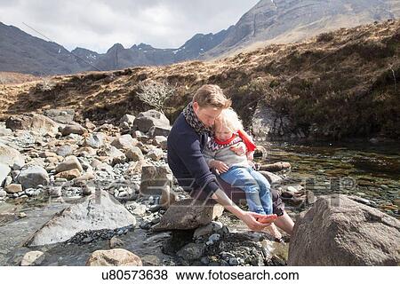 Stock Photo - Father and son sitting on rocks, Fairy Pools, Isle of Skye, Hebrides, Scotland. Fotosearch