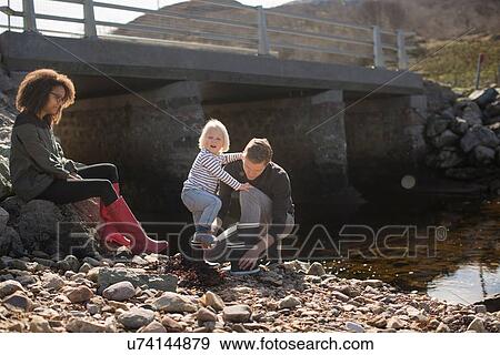 Father putting wellingtons on son by footbridge View Large Photo Image Stock Photo - Father putting wellingtons on son by footbridge. Fotosearch