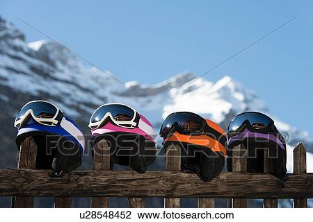 Stock Image - Four skiing helmets on wooden fence. Fotosearch