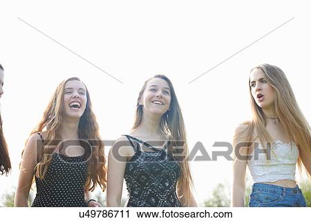 Stock Image - Four teenage girls laughing and chatting in park. Fotosearch