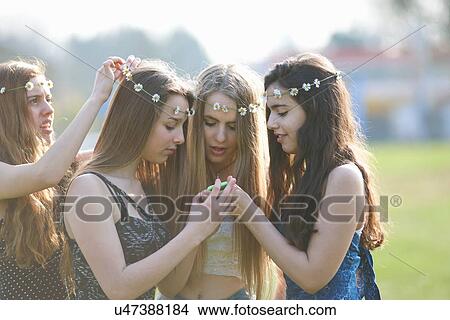 Four teenage girls wearing daisy chain headdresses reading smartphone texts in park View Large Photo Image Picture - Four teenage girls wearing daisy chain headdresses reading smartphone texts in park. Fotosearch