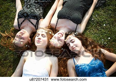 Stock Image - Four teenage girls wearing daisy chain headdresses lying on park grass. Fotosearch