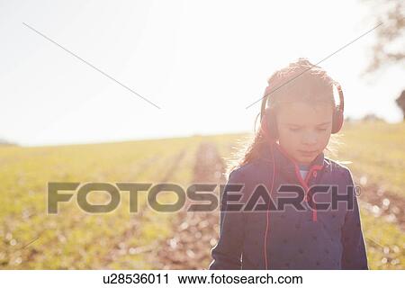 Stock Image - Girl strolling in field wearing headphones for metal detecting. Fotosearch