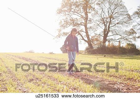 Stock Image - Girl wearing headphones using metal detector in sunlit field. Fotosearch