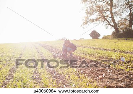 Picture - Girl with metal detector crouching and staring down in field. Fotosearch